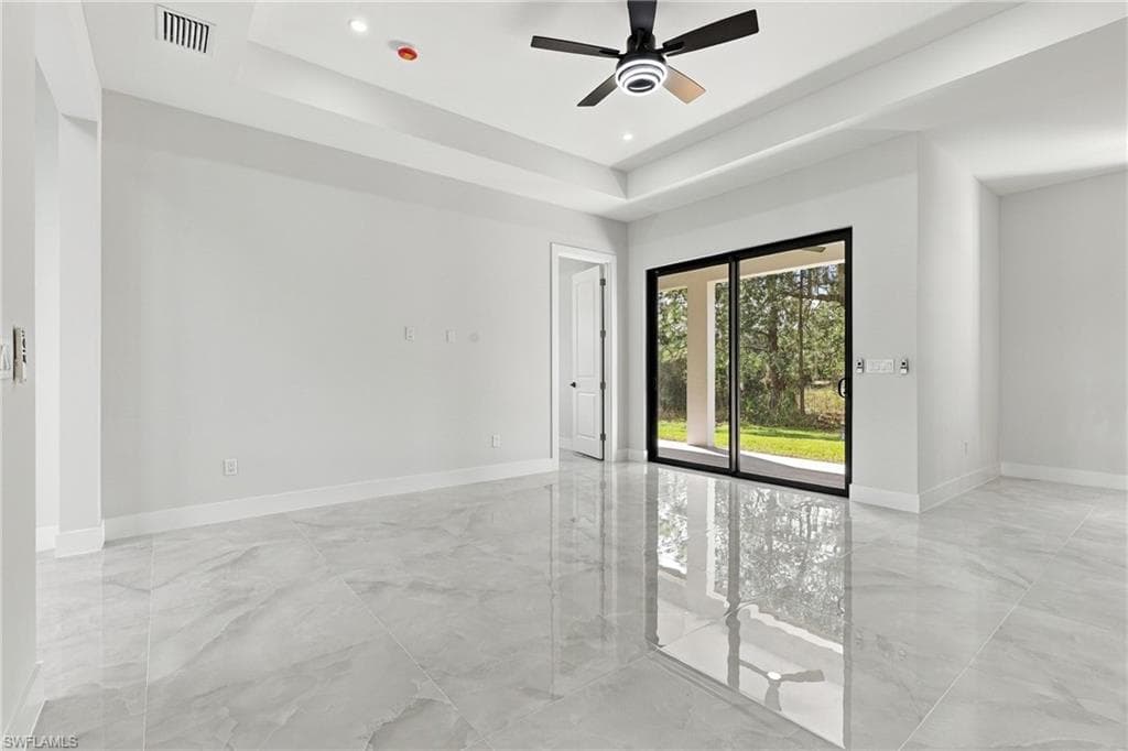 Spacious interior featuring a tray ceiling, ceiling fan with integrated lighting, and polished tile flooring