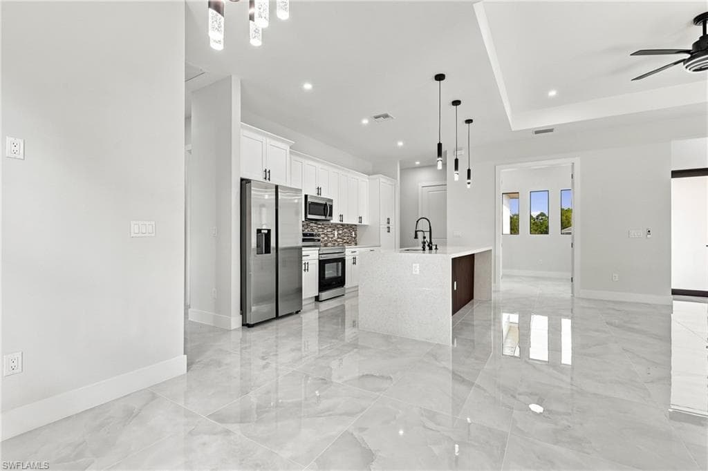 Open concept kitchen featuring stainless steel appliances, white cabinetry, a large kitchen island with pendant lighting, and polished stone-finish flooring