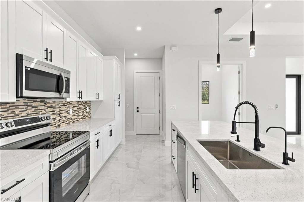 White cabinetry with matte black hardware, stainless steel appliances, mosaic tile backsplash, light-toned countertops, and an undermount sink with a matte black faucet
