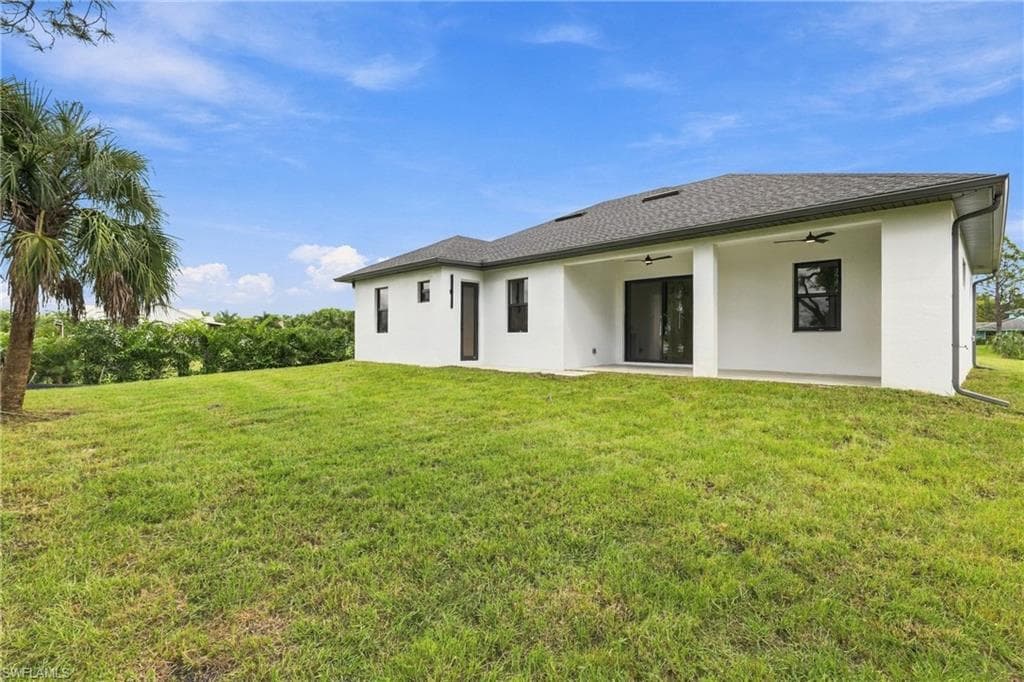 Spacious backyard featuring a covered patio, sliding glass doors, contemporary exterior lighting, and a dark shingle roof