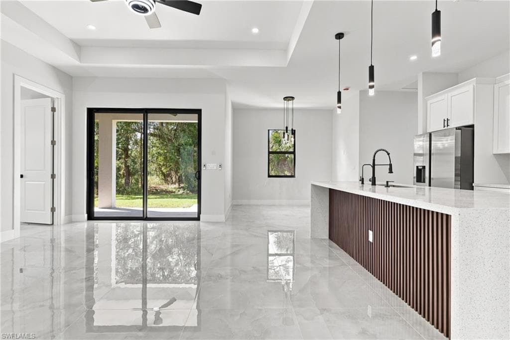 Polished tile flooring, tray ceiling, sliding glass doors, white cabinetry, and a kitchen island with a waterfall countertop