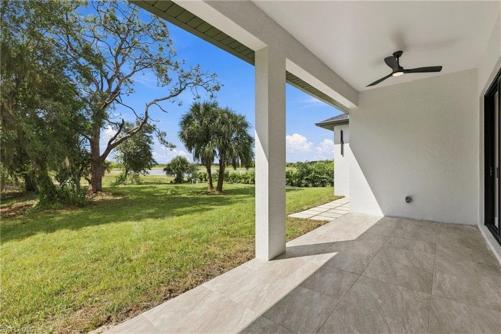 Covered patio with large format tile flooring, black ceiling fan, and expansive grassy area