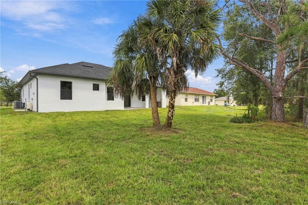 Spacious grassy yard with mature trees, featuring a white stucco exterior and dark framed windows