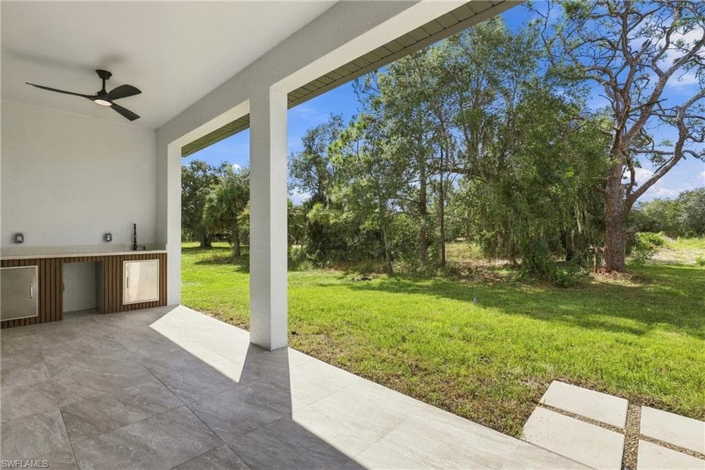 Covered patio featuring a built-in outdoor kitchen, ceiling fan, and large format tile flooring
