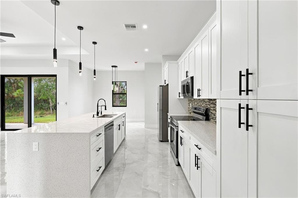 Modern kitchen featuring a large island with an integrated sink, white shaker cabinetry with matte black hardware, stainless steel appliances, and tile flooring