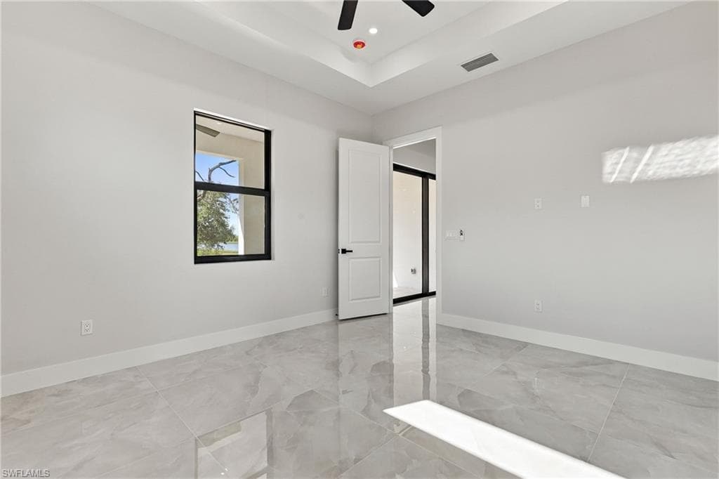 Tray ceiling, recessed lighting, ceiling fan, large format tile flooring, and a white interior door with black hardware