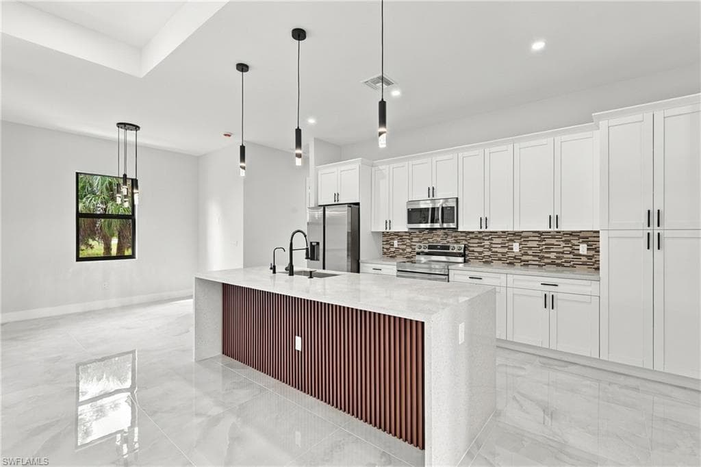 Kitchen featuring an island with a slatted wood-finish panel, white shaker-style cabinetry, stainless steel appliances, and a tiled backsplash