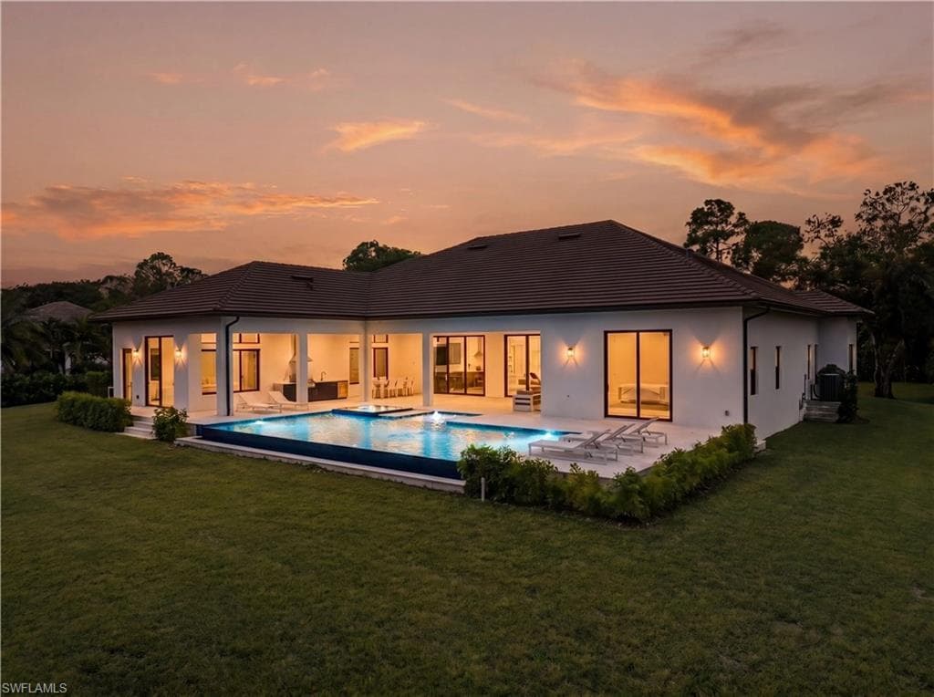 Contemporary residence featuring a large pool, covered patio, outdoor lighting, expansive lawn, and mature landscaping