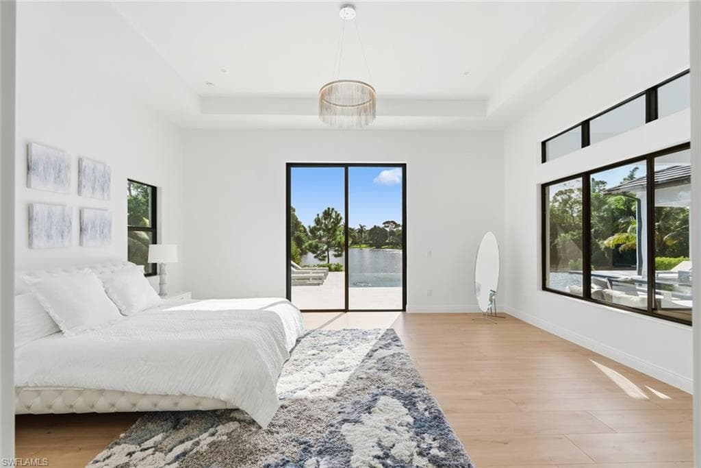 Tray ceiling with a decorative light fixture, large sliding glass doors, multiple windows with black trim, and wood-finish flooring
