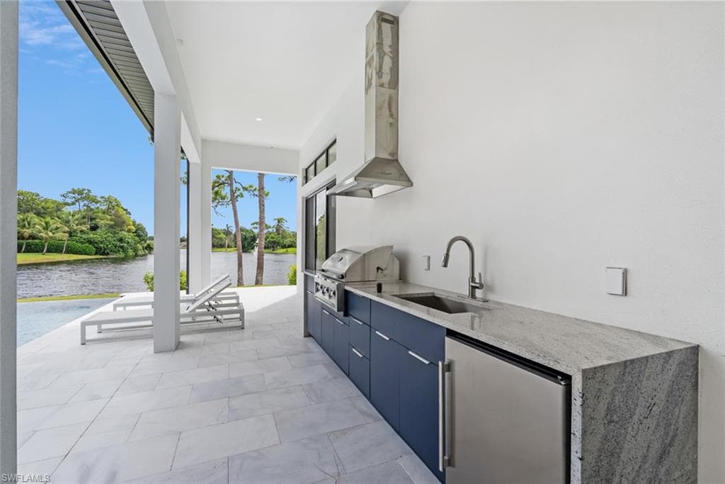 Outdoor kitchen with built-in grill, stainless steel range hood, stainless steel beverage refrigerator, and granite countertops