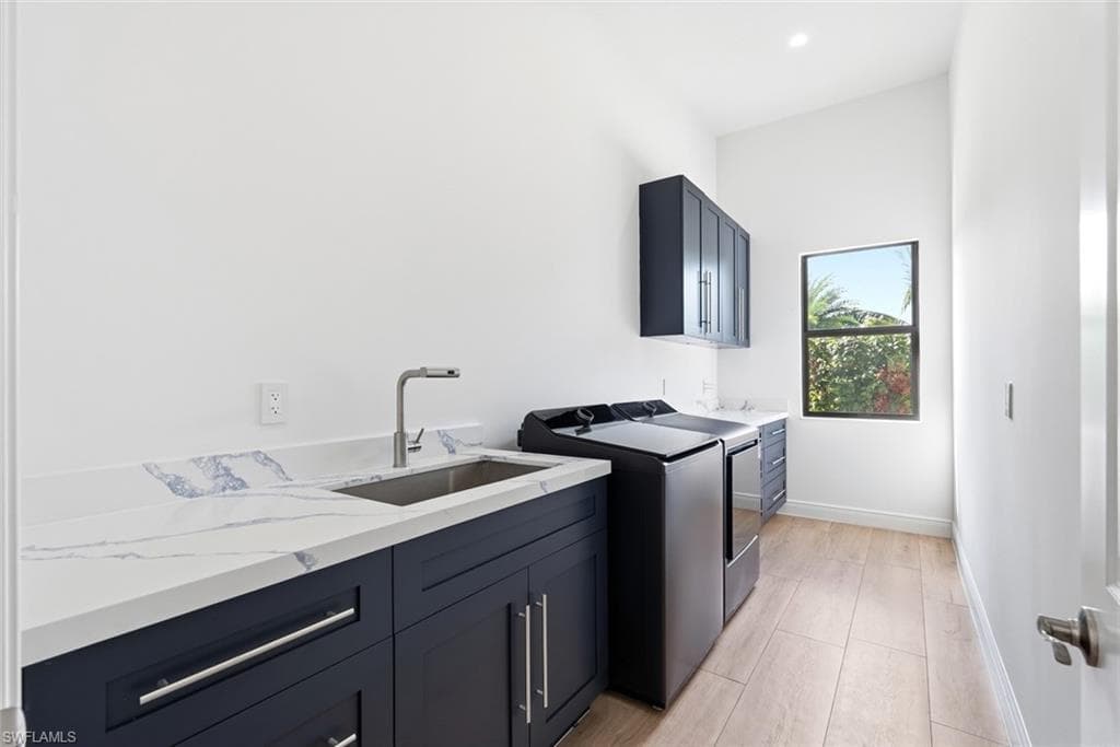 Laundry room with a built-in utility sink, dark cabinetry, and light wood-finish flooring