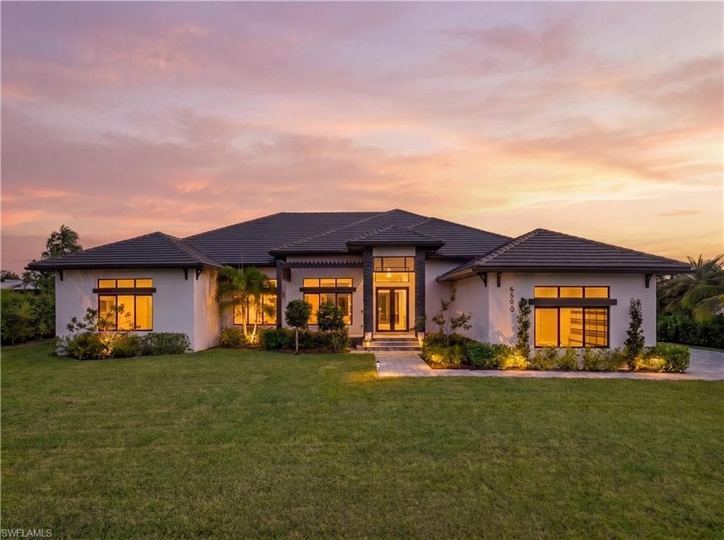 Modern architecture featuring a dark tile roof, white stucco exterior, prominent entry, and extensive front landscaping