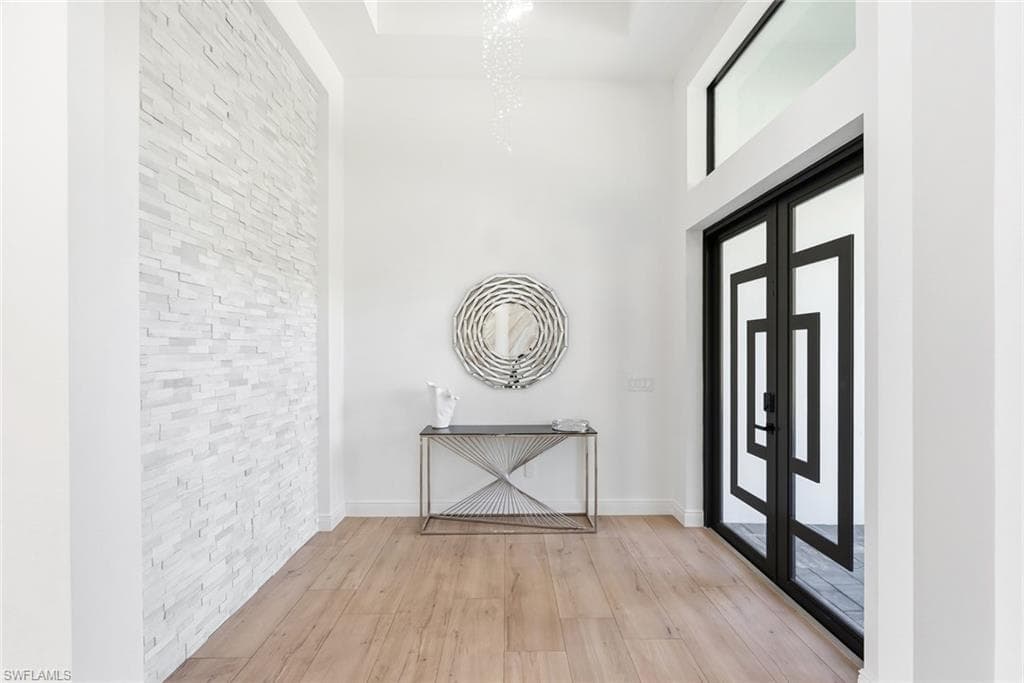Entryway featuring a stacked stone accent wall, wood-finish flooring, a contemporary chandelier, and double entry doors with decorative framing and transom window