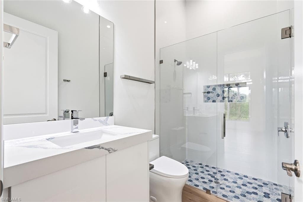 White vanity with an integrated sink and chrome faucet, frameless glass shower enclosure, blue and white hexagonal tile shower floor, and a built-in shower niche with blue and white mosaic tiling
