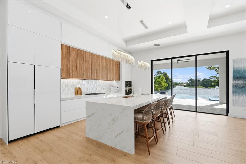 Gourmet kitchen with sleek white and wood-finish cabinetry, a waterfall-edge island, and wood-finish flooring
