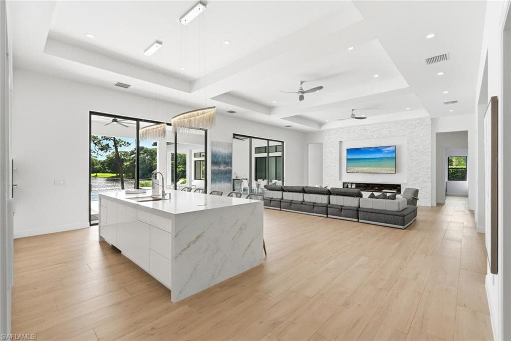 Open-concept living space with light wood-finish flooring, a kitchen island featuring a waterfall countertop, and sliding glass doors