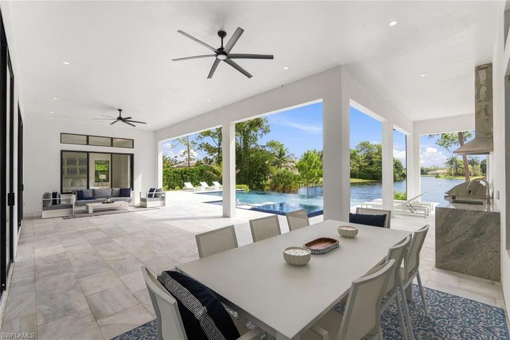 Expansive covered patio with large format tile flooring, multiple ceiling fans, and an outdoor kitchen featuring a built-in grill and range hood